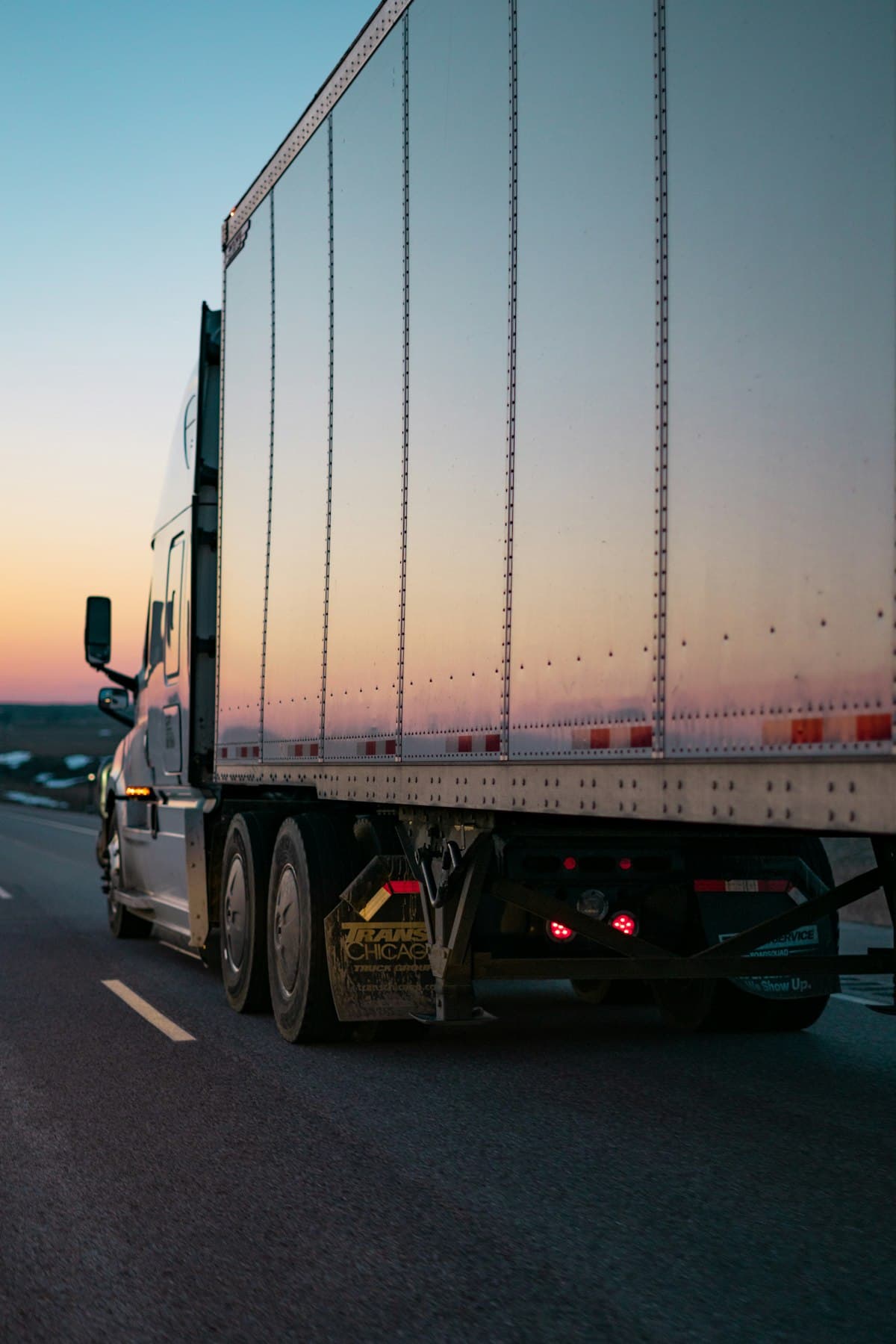 White freight semi truck on a highway at dusk with a dramatic sky